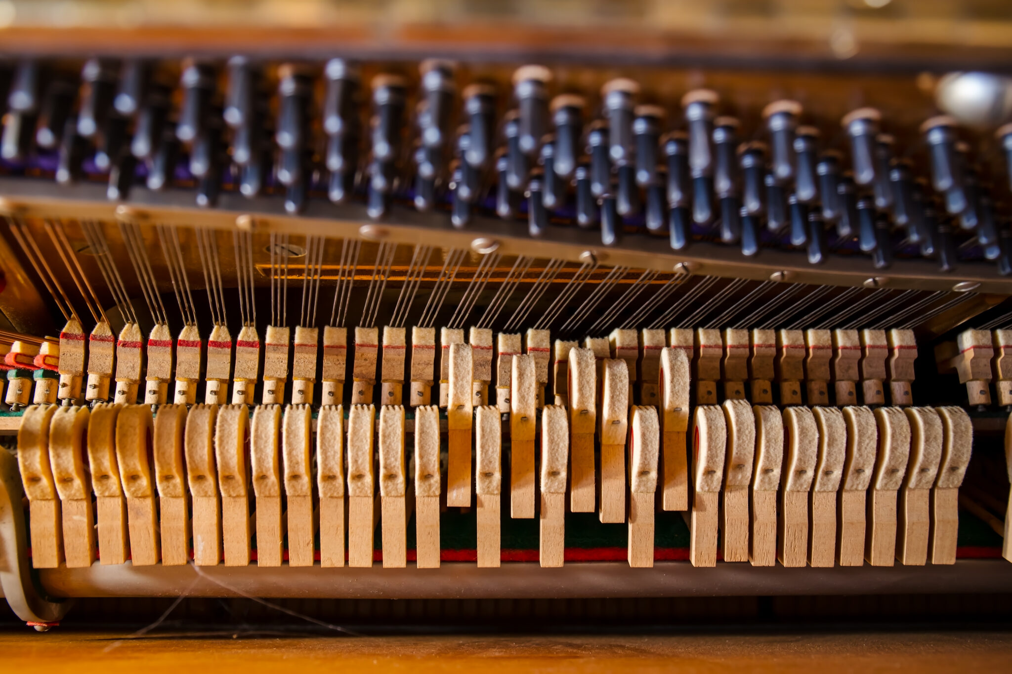 Close-up of an upright piano’s action showing wooden hammers, strings, and tuning pins.